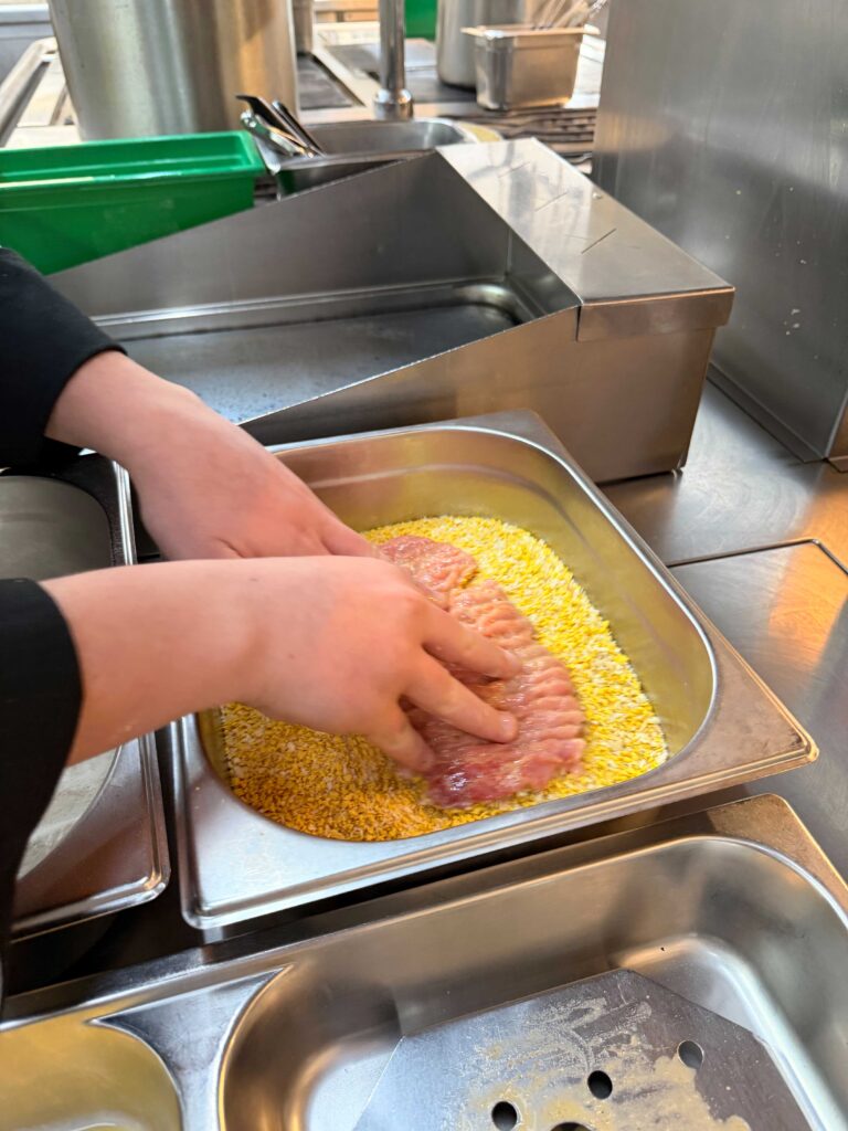 Kind beim panieren eines Schnitzels